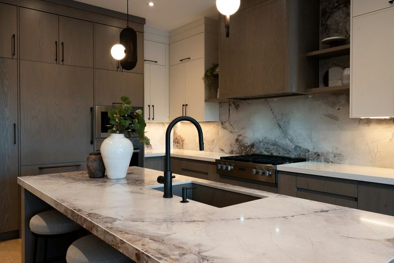 Veined white stone island with a black faucet against dark wood cabinetry